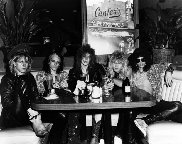 Guns N Roses band members sitting around a table inside a restaurant in black and white image