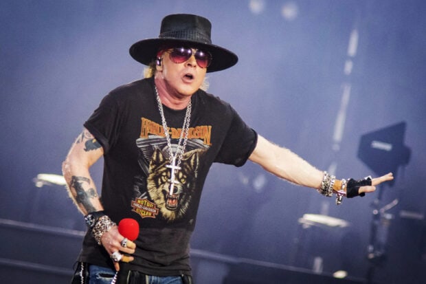 Axl Rose performing live on stage wearing a black hat and Harley Davidson shirt