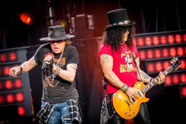 Guns N Roses band performing live on stage with lead singer and guitarist wearing hats and casual clothes