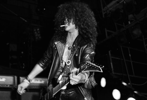 Guns N Roses guitarist playing on stage with curly hair and leather jacket