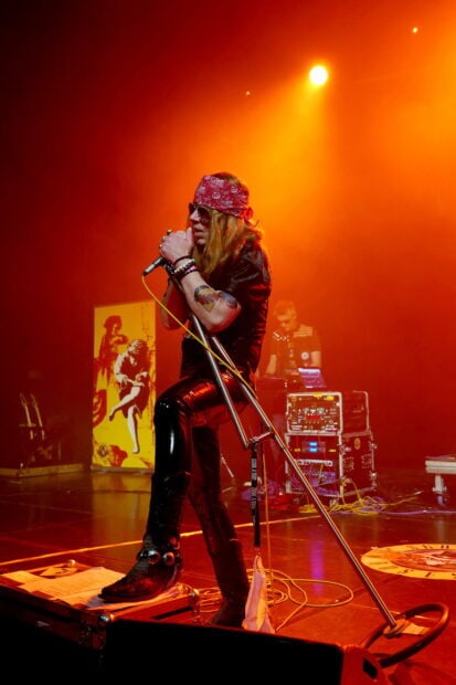 Axl Rose singing on stage with a microphone stand and wearing a red bandana