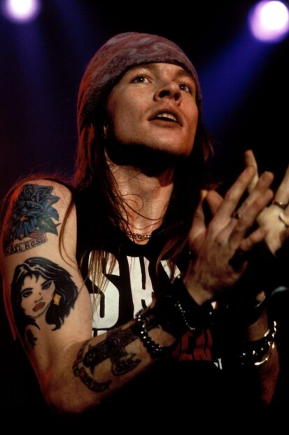 Axl Rose from Guns N Roses performing on stage with detailed tattoos on his arm