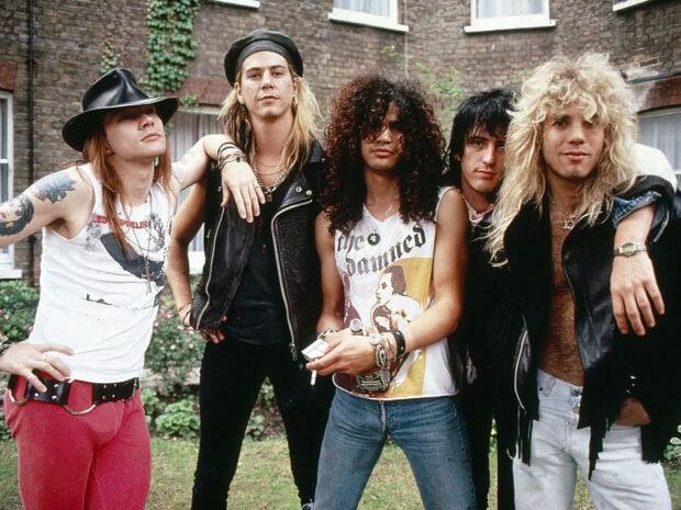 Guns N Roses band members posing outdoors in casual rock attire with tattoos and vintage hairstyles