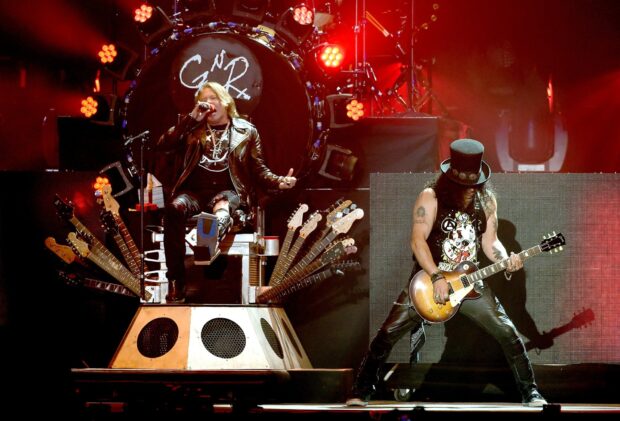 Guns N Roses band performing live on stage with multiple guitars and dynamic lighting