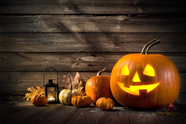 A group of Halloween pumpkins with glowing faces and autumn leaves on wooden floor, HD Desktop Wallpaper