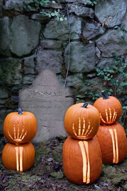 Halloween pumpkins with skeleton hand carvings stacked near a stone gravestone, HD Mobile Wallpaper