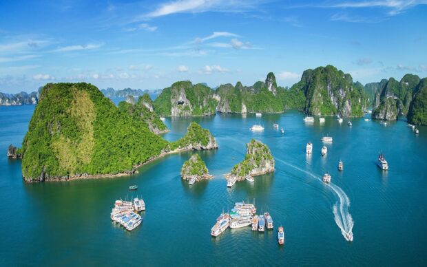 A panoramic view of Halong Bay with green limestone islands and boats sailing on clear blue water