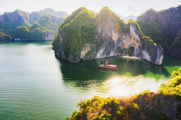 A traditional junk boat sailing near limestone karsts in Halong Bay with lush greenery and calm water