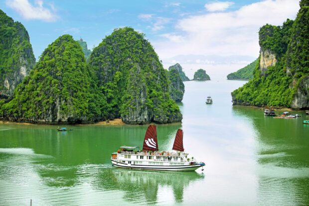 A traditional Vietnamese junk boat sailing through lush green limestone islands in Halong Bay