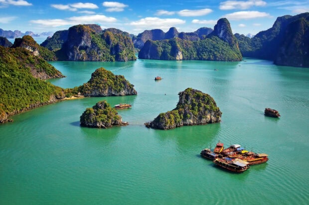 Halong Bay with green islands and boats on turquoise water under a blue sky