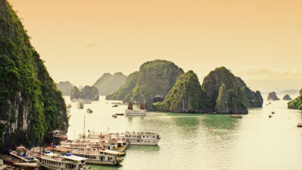 Limestone formations in Halong Bay with boats sailing on calm waters during sunset