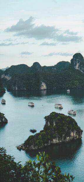 Lush green islands in Halong Bay with calm blue water and several boats floating around