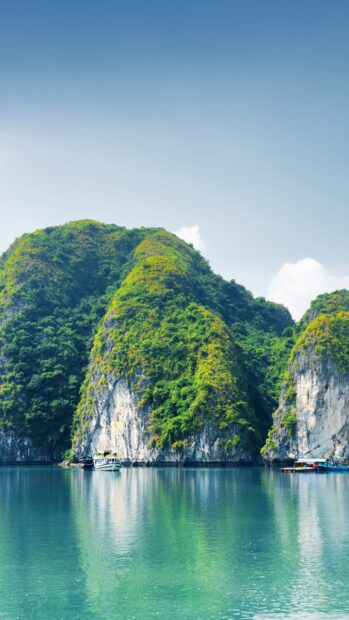 Lush green mountains of Halong Bay with calm water and boats in view