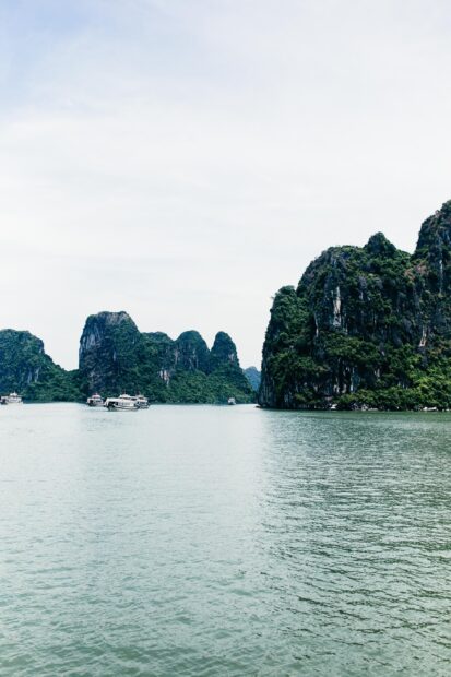 Limestone islands in Halong Bay with boats floating on the water under a cloudy sky
