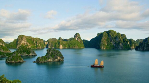 A traditional boat sailing through Halong Bay with lush green islands and calm water