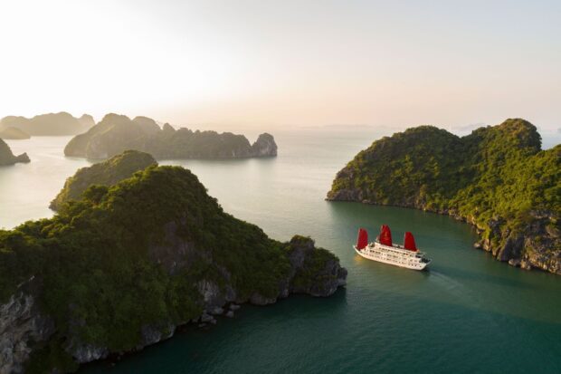 A scenic view of Halong Bay with green islands and a cruise ship sailing through calm waters