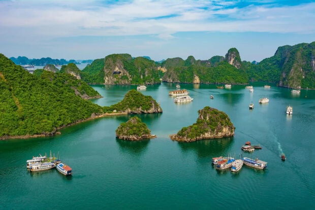 A scenic view of Halong Bay with lush green islands and multiple boats sailing on turquoise water