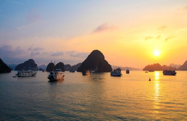 Beautiful limestone islands at Halong Bay during sunset with several boats on the water