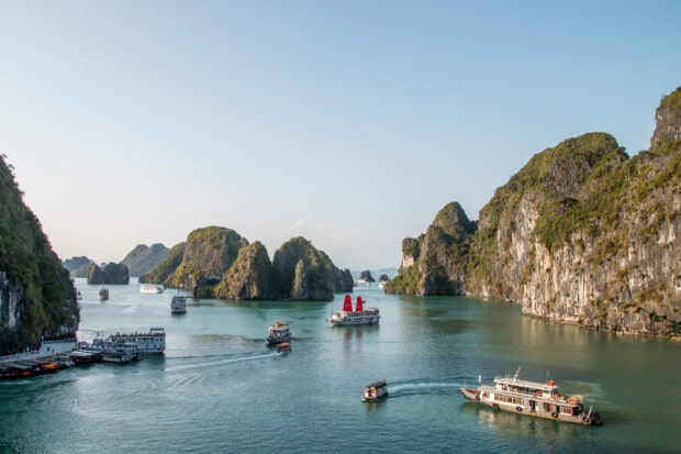 Halong Bay with limestone islands and boats sailing on calm water at sunset