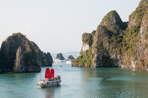 Traditional sailing boat with red sails in Halong Bay landscape with rocky islands and calm water