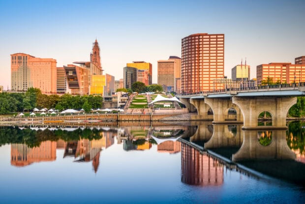 Hartford skyline with city buildings and bridge reflected in the calm river under clear sky