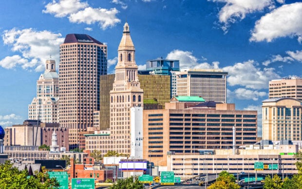 The Hartford skyline features diverse historic and modern buildings under a bright blue sky with clouds