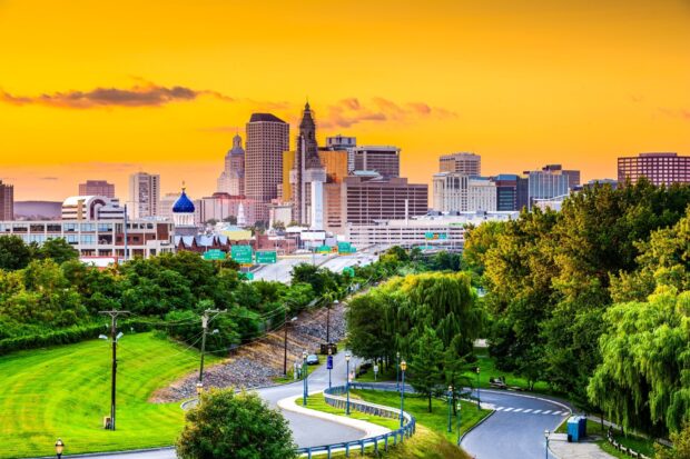 A vibrant Hartford cityscape with skyscrapers and lush greenery under a bright sunset sky