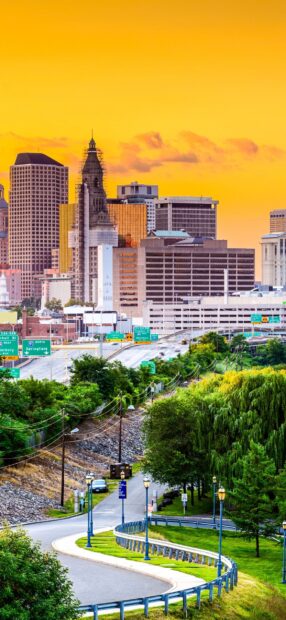 A scenic view of Hartford skyline with greenery and a winding road under a bright sky