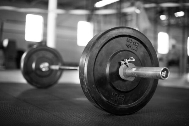 A heavy barbell with 45 lb weights rests on a gym floor ready for Crossfit workouts, 2K Desktop Wallpaper