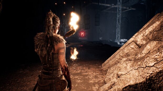 A Hellblade character explores a dark cave holding a burning torch, 4K Desktop Wallpaper