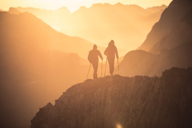 Two hikers trekking on rocky mountain ridge during sunset with warm light