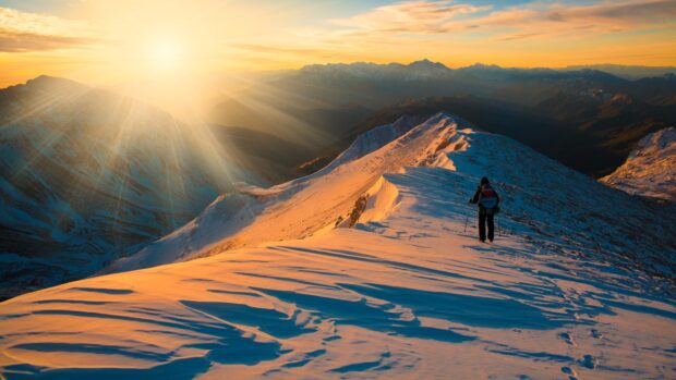 A hiker walking on snowy mountain ridge during golden sunset light