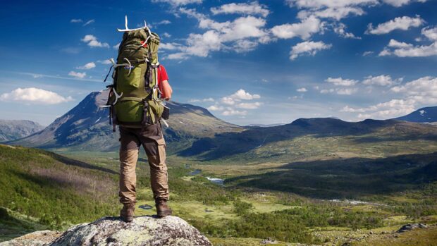 Hiker with a large backpack enjoying the mountain view on a sunny day hiking