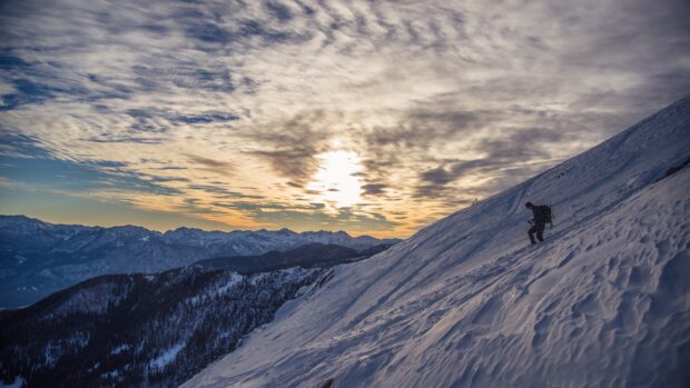 A hiker climbing a snowy mountain slope during sunset in the highlands