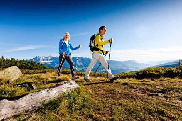 Two hikers walking on a mountain trail with trekking poles and scenic landscape in the background