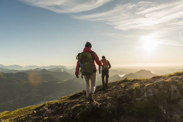 Two hikers with backpacks walking on a mountain trail during sunset