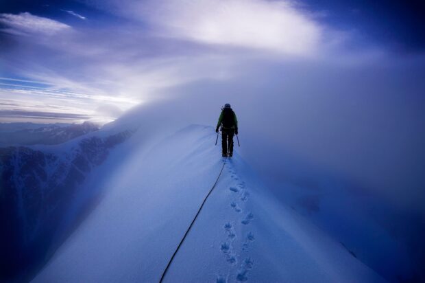 A hiker trekking along a snowy ridge surrounded by mountain peaks and fog