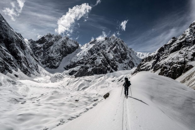 A hiker trekking through snowy mountains under a cloudy sky