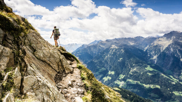Hiker trekking along a mountain trail surrounded by rocky cliffs and green valleys