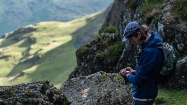 Hiker checking watch during mountain hiking trip with rocky terrain and green hills in background