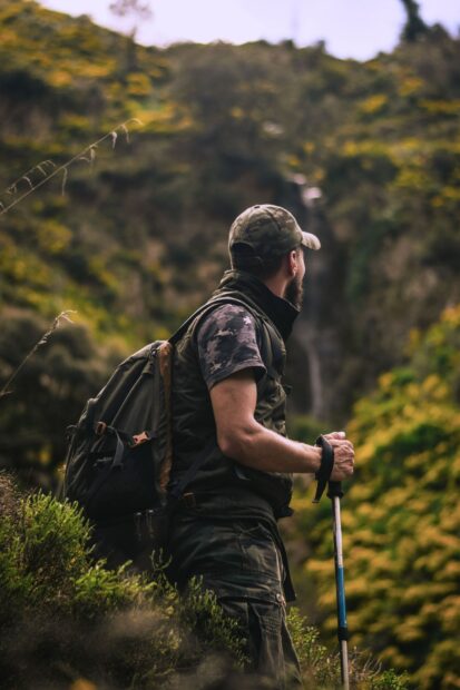 A man with a backpack hiking with a trekking pole in a green forest