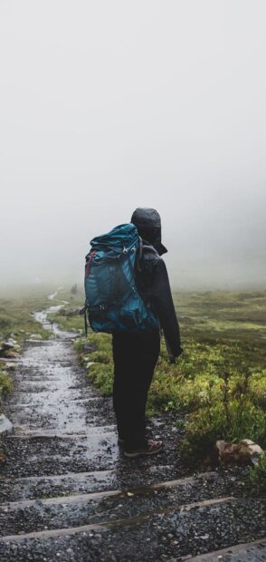 A hiker with a large backpack walking on a misty mountain trail