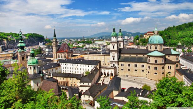 The Austria cityscape features historic buildings and lush greenery under a bright blue sky, 2K Desktop Wallpaper