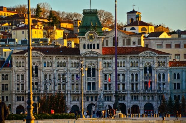The historic architecture of Trieste shines warmly at sunset with people walking nearby, 2K Desktop Wallpaper