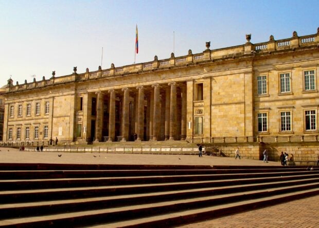 This photo shows a historic building with the Colombian flag in Bogota featuring steps and people around