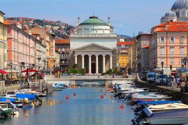 The view of a historic canal and church in Trieste showcases beautiful buildings and boats along the water, HD Desktop Wallpaper