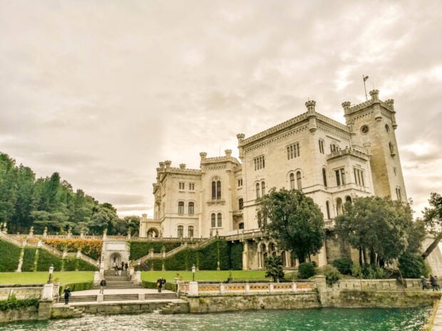 A historic castle stands by the waterfront surrounded by greenery in Trieste showcasing impressive architecture, 2K Desktop Wallpaper
