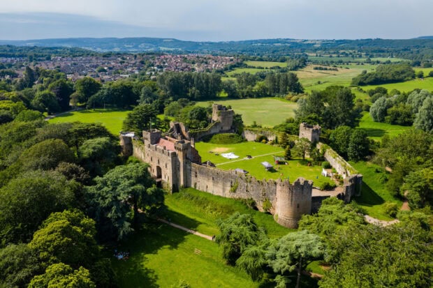 Aerial view of a historic castle surrounded by lush greenery in Wales showing expansive fields and distant hills, 2K Desktop Wallpaper
