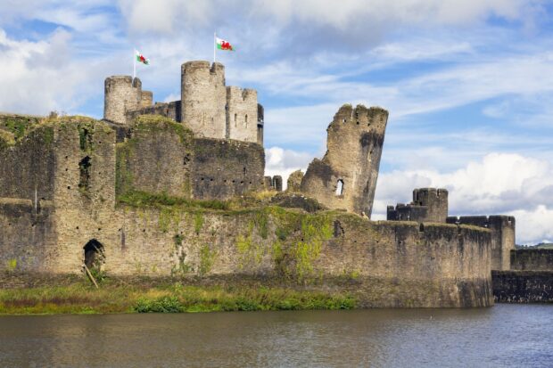 A historic stone castle with Welsh flags overlooks the water in Wales, 2K Desktop Wallpaper
