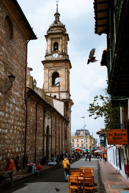 A historic clock tower stands tall in Bogota with people walking nearby on a cloudy day, HD Mobile Wallpaper
